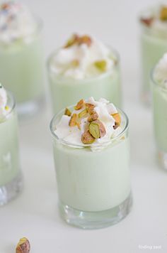 small desserts with whipped cream, pistachio and nuts in them on a white table