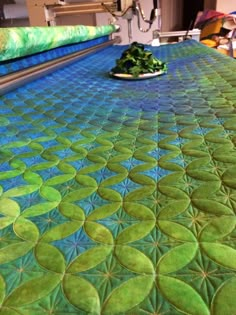 a close up of a quilt on a bed with green circles in the middle and blue background