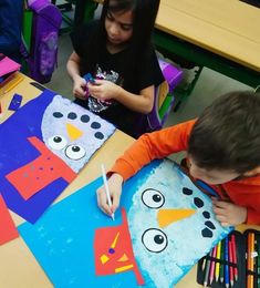 two children are sitting at a table making paper snowmen with colored crayons