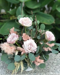 a bouquet of pink flowers sitting on top of a stone wall next to green leaves