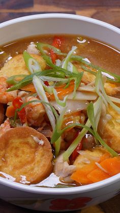 a bowl filled with soup and vegetables on top of a wooden table next to a spoon