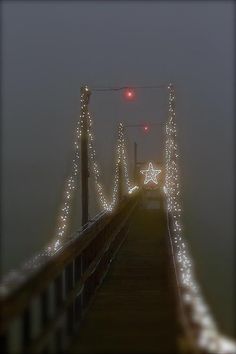 a long bridge with lights on it and a red traffic light at the top in the fog