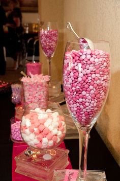 a table topped with lots of pink and white candies next to two wine glasses