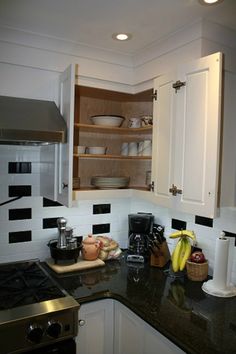 a kitchen with white cabinets and black counter tops, an open shelf above the stove