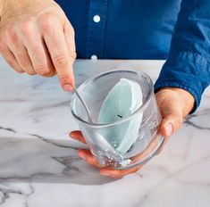 a person holding a glass with some kind of substance in it on a marble table