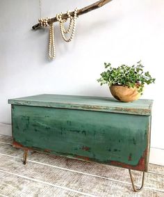 a green chest with a plant on top and a rope hanging from the wall above it