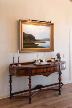 a painting hangs on the wall next to a table with two candles and an empty tray