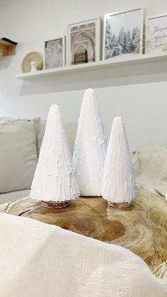 three small white trees sitting on top of a tree stump in front of a bed