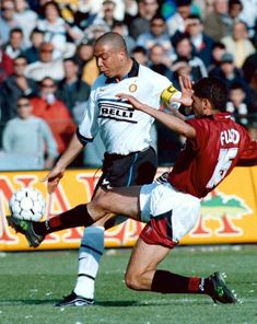 two men are playing soccer in front of an audience at a sporting event, one is about to kick the ball