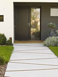 the front entrance to a modern home with grass and shrubs