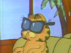 a cat wearing sunglasses sitting on top of a couch in front of a palm tree