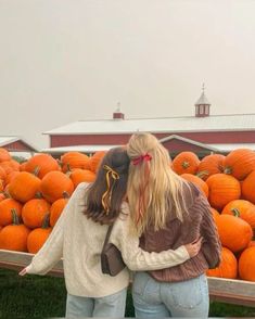 two women standing in front of a pile of pumpkins with their arms around each other