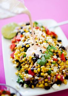 a white plate topped with corn, black beans and cilantro sauce next to a lime wedge