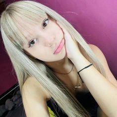 a woman with long blonde hair sitting in front of a purple wall and looking at the camera