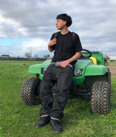 a young man sitting on top of a green four wheeled vehicle in a grassy field