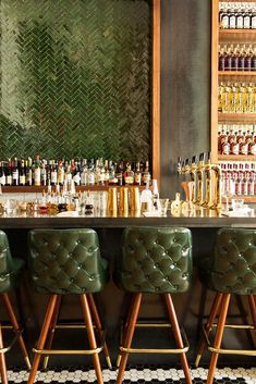 a bar with stools and bottles on the wall behind it in front of a mirror