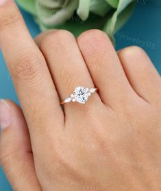 a woman's hand with a diamond ring on top of her finger and flowers in the background