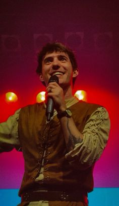 a man holding a microphone in his right hand and singing into the microphone on stage