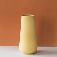 a yellow vase sitting on top of a white table next to an orange wall in the background