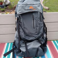 a back pack sitting on top of a striped rug next to a wooden fence and grass