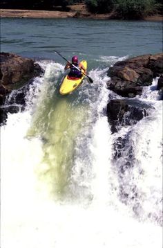 a man riding on top of a yellow kayak down a river surrounded by rocks