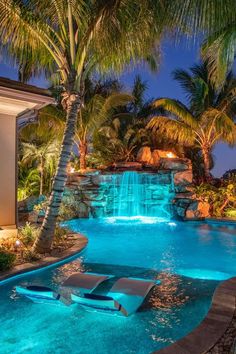 an outdoor swimming pool surrounded by palm trees and water features a waterfall at the end