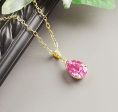 a necklace with a pink stone hanging from it's gold plated link chain