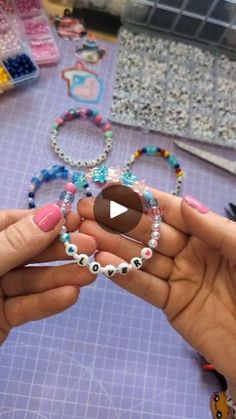 two hands holding bracelets and beads on a table with other crafting supplies in the background