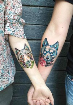 two people are holding hands with tattoos on their arms and one has a dog's head