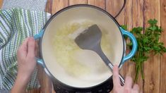 a person is stirring some food in a pot with a spoon and parsley on the side