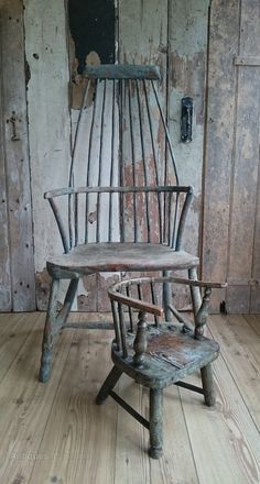 an old rocking chair and foot stool in front of a wooden wall with peeling paint