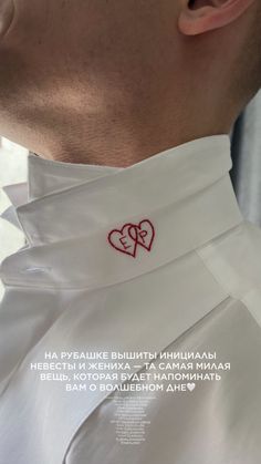 a close up of a person wearing a white shirt with two hearts on the collar