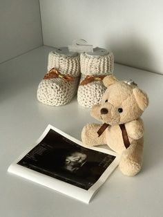 a teddy bear sitting next to two crocheted baby booties and a book