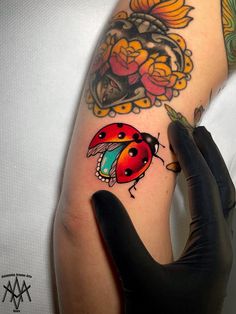 a ladybug tattoo on the left arm and right hand with black gloves holding it