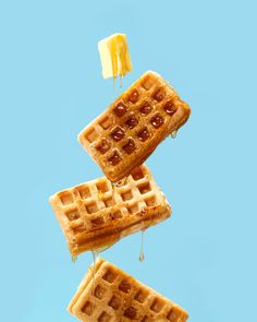 three waffles with syrup and butter on them floating in the air against a blue background