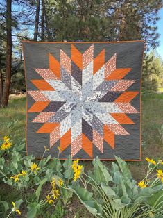 an orange and gray quilted star on display in the grass with yellow flowers around it