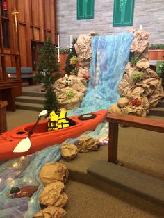 a red kayak is in the middle of a room with rocks and water flowing from it