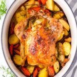 a close up of a chicken in a pot with potatoes and carrots on the side