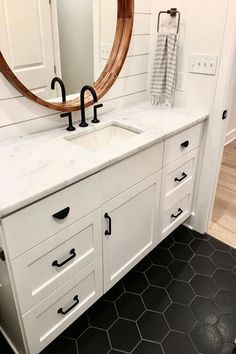 a bathroom with black and white flooring and a large round mirror above the sink