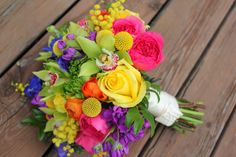 a bridal bouquet is sitting on a wooden table with purple, yellow and orange flowers