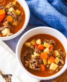 two white bowls filled with meat and vegetable soup on top of a wooden table next to a blue towel