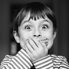 a young boy making a funny face with his hands on his mouth and eyes wide open