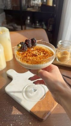 a person holding up a dessert in a glass bowl on top of a wooden table