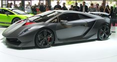 a grey sports car is on display at an auto show with people standing around it