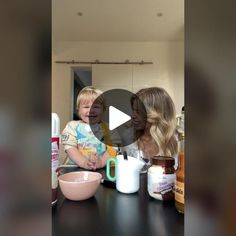 a woman holding a child in front of a counter with food and milk on it