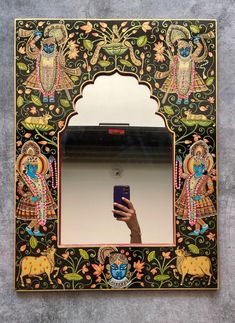 a hand holding a cell phone in front of a mirror with an ornate design on it