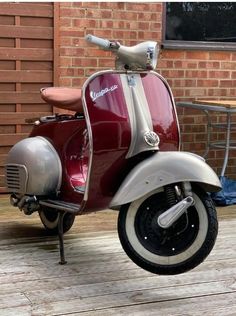 a red scooter parked on top of a wooden floor next to a brick building