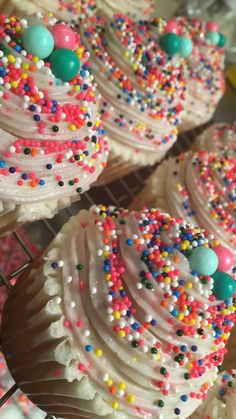 cupcakes with white frosting and colorful sprinkles are on display