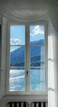 two windows with white curtains and mountains in the background, one is open to see water