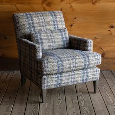 an upholstered chair sits on a wooden floor in front of a wood paneled wall